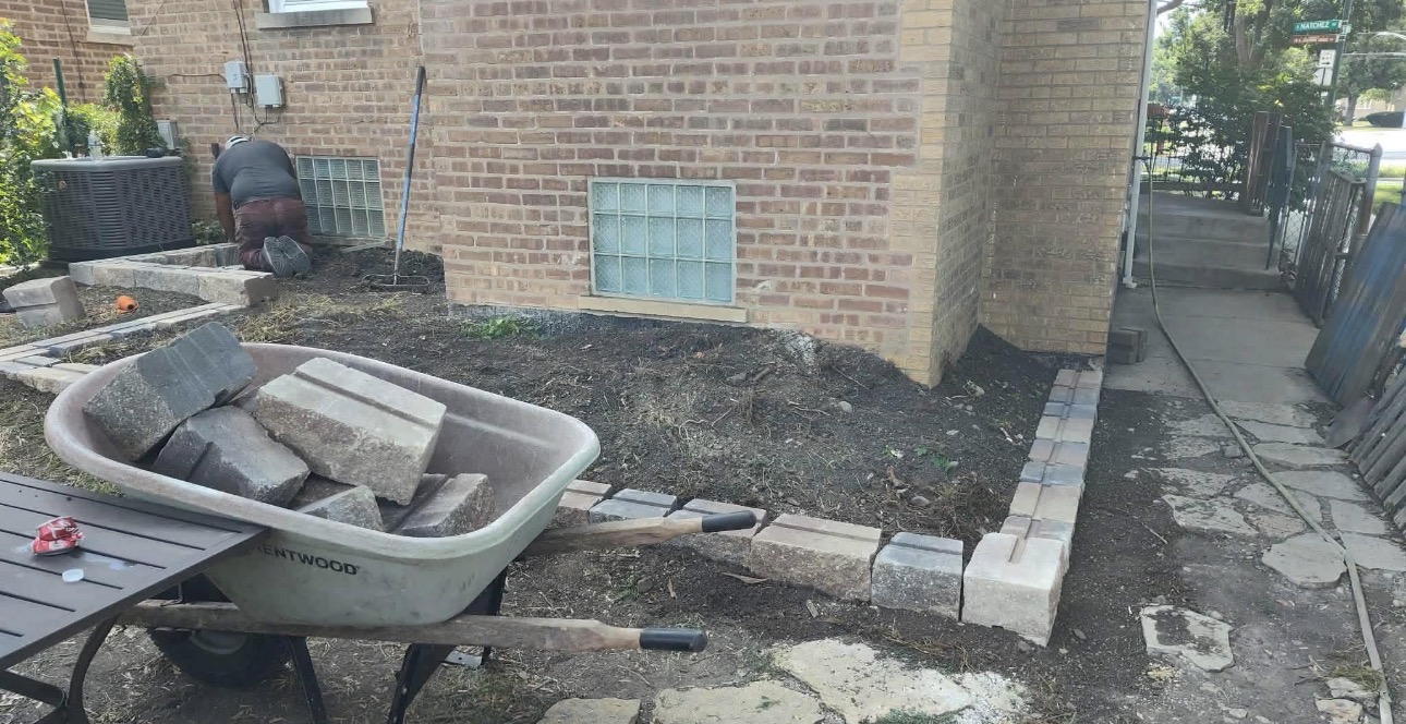 Bare dirt side yard before landscaping with wheelbarrow of pavers