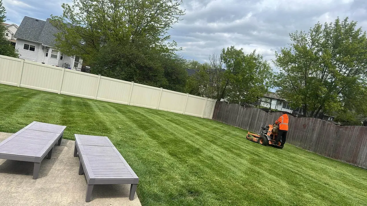 Crew member on a stand-on mower cutting a large fenced backyard lawn