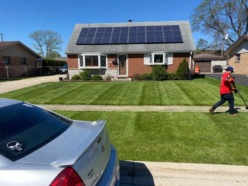 Crew member trimming a striped front lawn at a brick home
