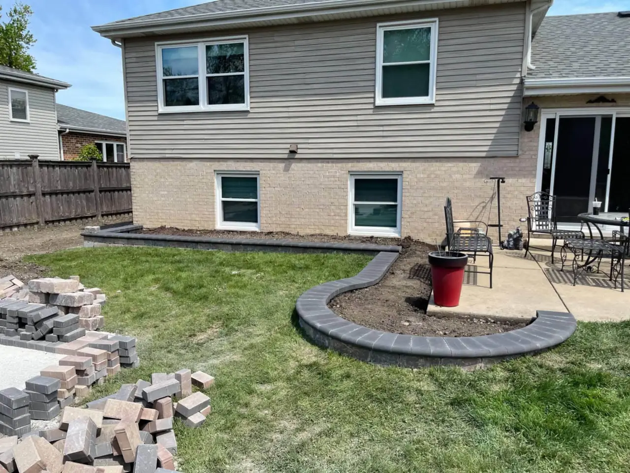 Charcoal paver border curving around a backyard patio during installation
