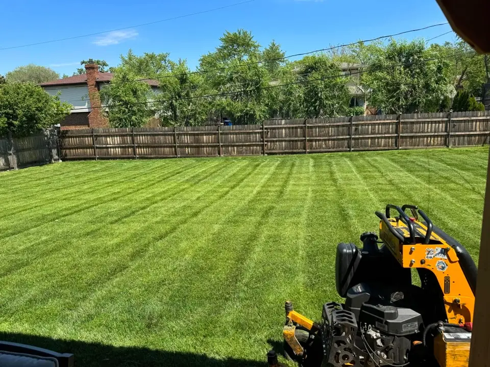 Large fenced backyard with fresh mowing stripes and a stand-on mower